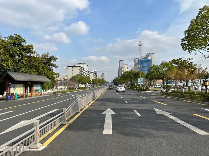 A wide tree-lined boulevard with a pavilion bus shelter and city towers in Jurong