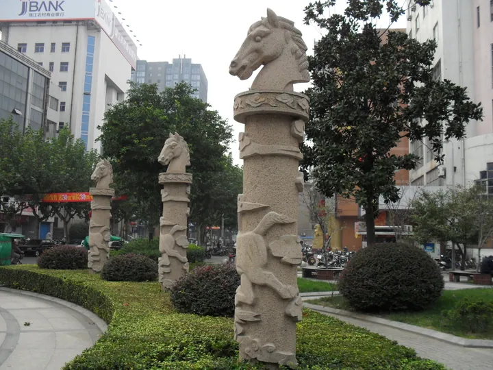 Carved stone pillars topped with horse heads in a landscaped street median in Jingjiang