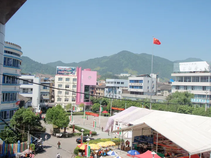 An elevated view of a town square with market tents, buildings and forested mountains in Taishun County