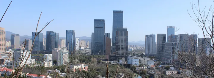 A city skyline of high-rise towers with hills behind, seen from a park