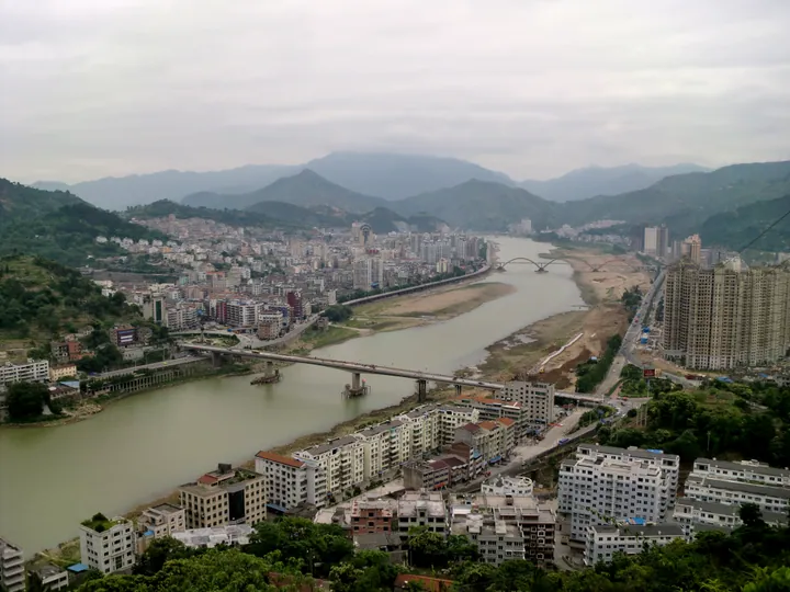 A riverside town with bridges and apartment towers set among mountains in Qingtian County