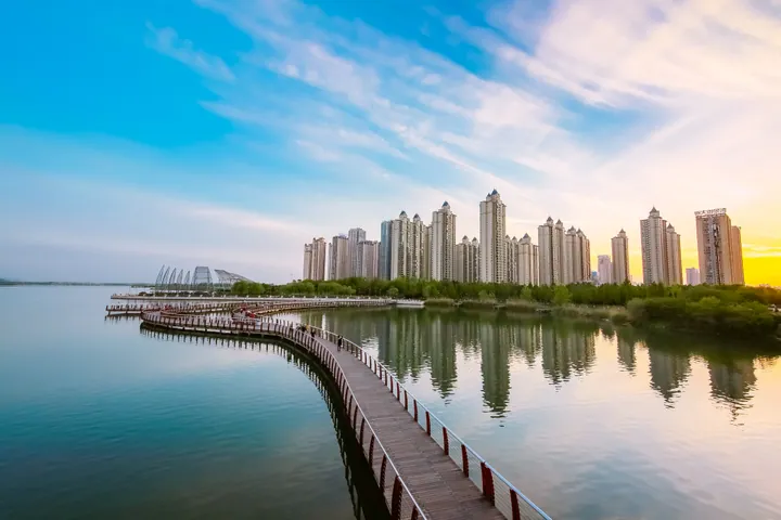 A lake, wooded hill and pagoda with a bridge and city skyline at sunset in Bengbu