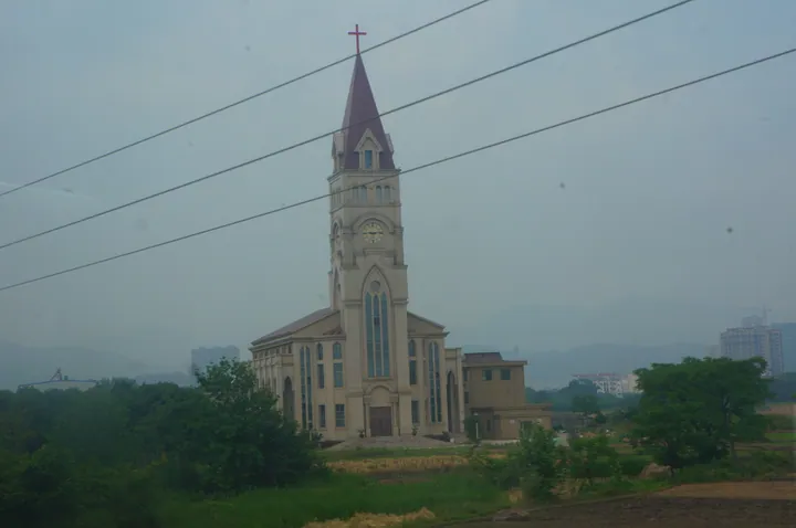 A tall stone church with a clock tower and spire, seen across fields