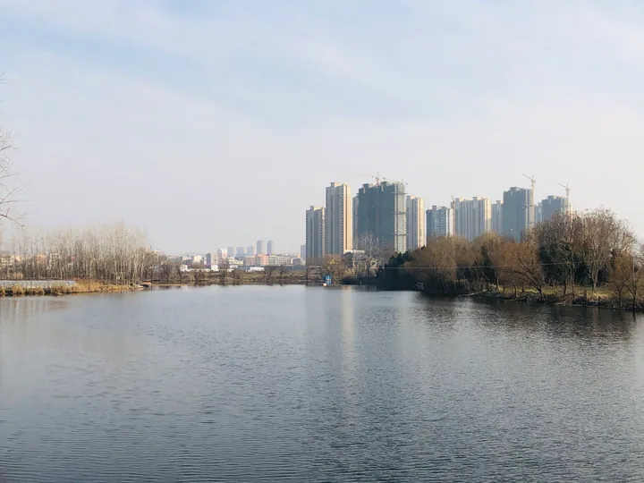 A river with apartment towers and bare trees on the far bank in Linquan County