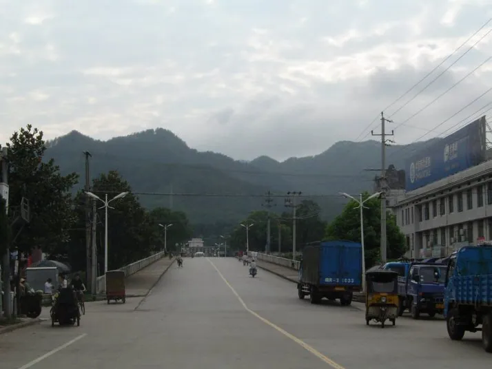 A wide street leading toward green mountains with a truck parked at the roadside