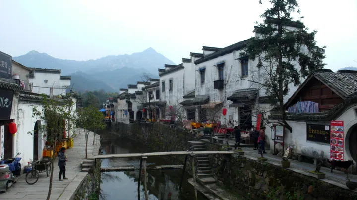 A traditional whitewashed village street beside a canal with mountains behind