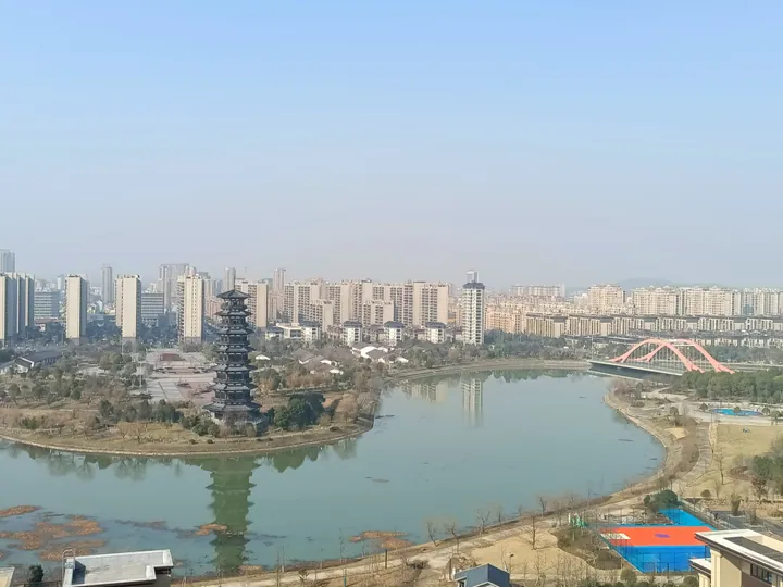 City skyline with a tiered black pagoda beside a lake and red arch bridge