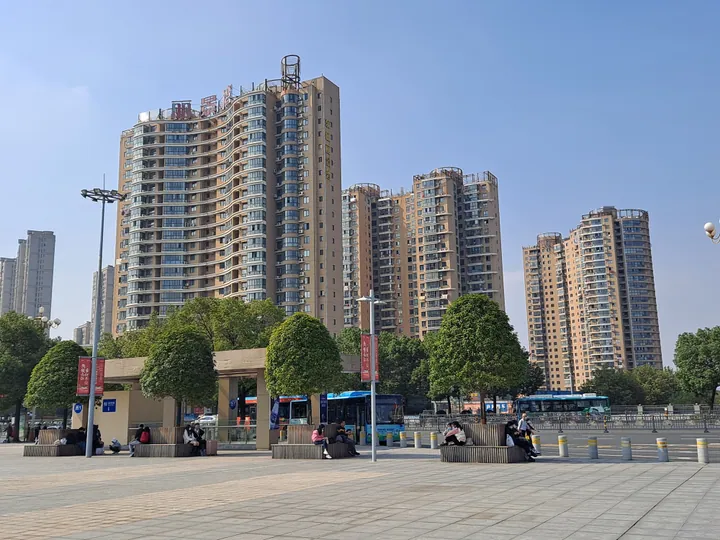Apartment towers and a plaza with a bus in front of a railway station in Jiujiang, China