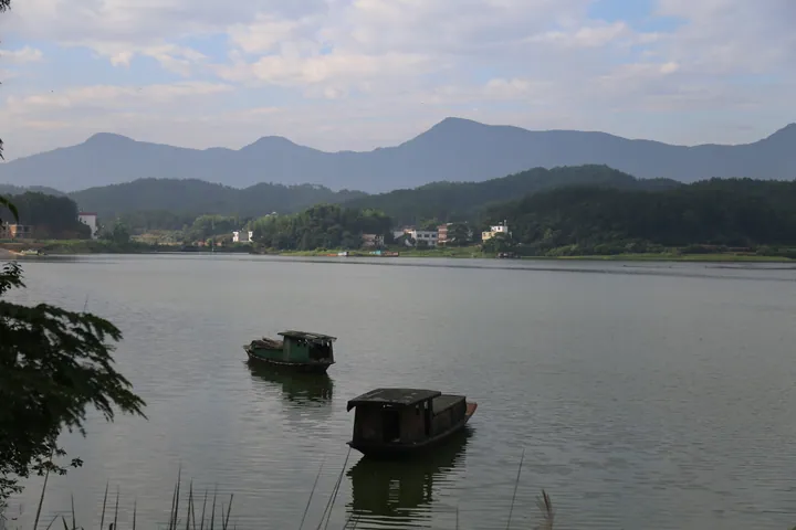 Wooden boats on a lake with hills and a lakeside village in Wuning County