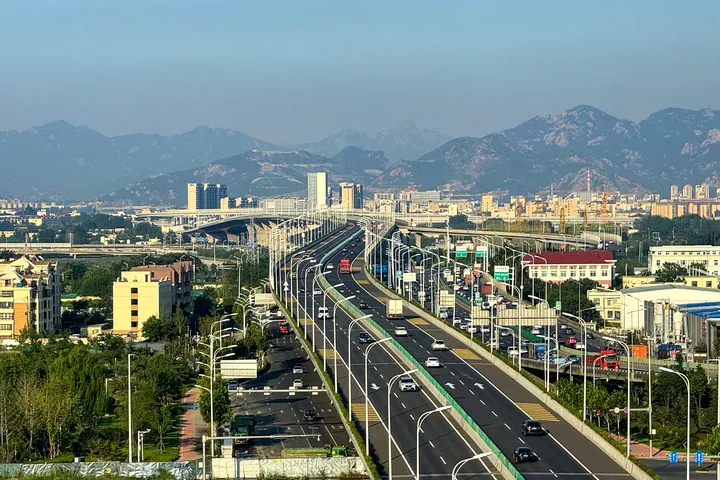 A multi-lane expressway running toward a city skyline with mountains behind