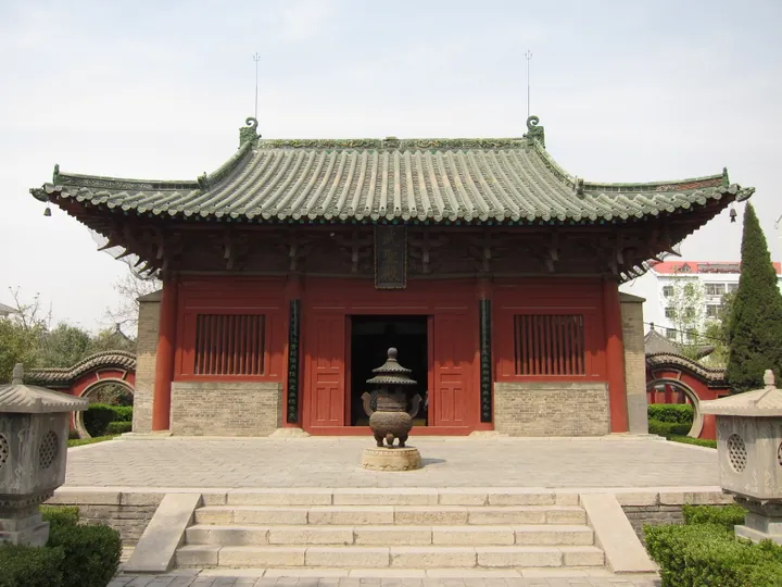 A red and green traditional Chinese temple hall with an incense burner in the courtyard