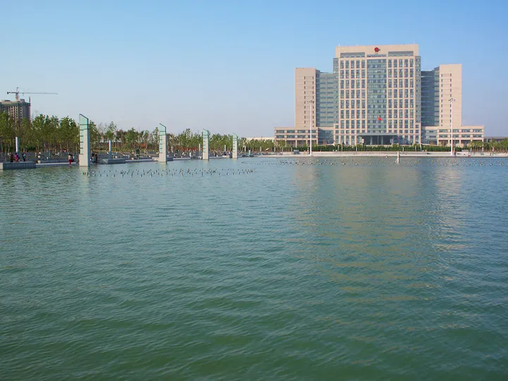 A large government building reflected in a fountain pool in Longkou