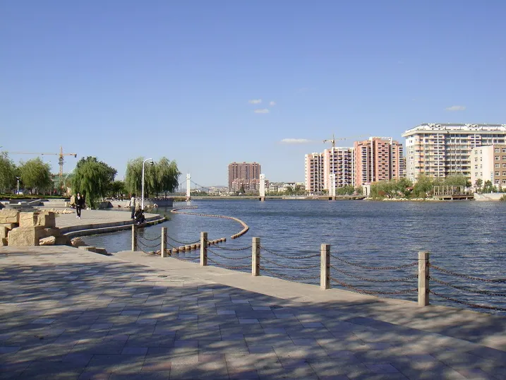 A lakeside park promenade with willow trees and the city skyline across the water in Zhaoyuan
