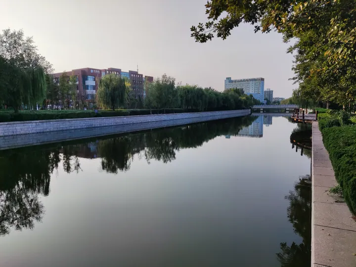 A calm river lined with willow trees and reflected buildings, Hanting District