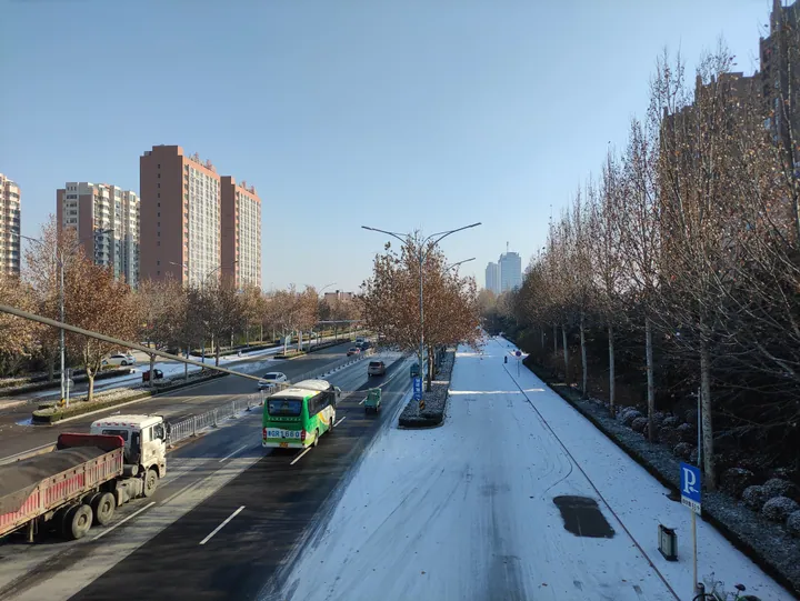 A snow-dusted city street with buses, trucks and apartment towers in Shouguang