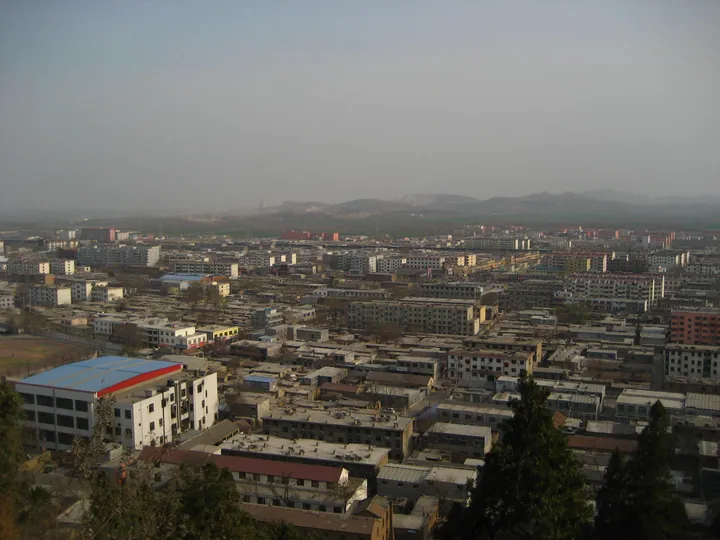 Rooftops of Jiaxiang town seen from a hillside, with hills in the distance