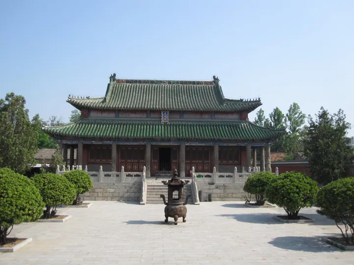 A traditional Chinese temple hall with a green tiled roof and a bronze incense burner