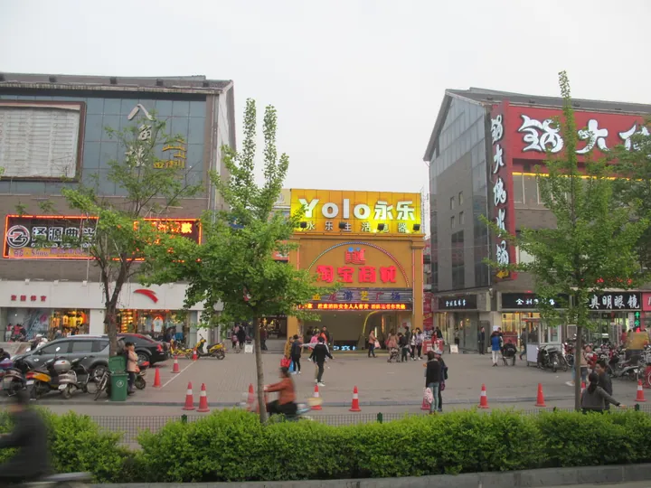 A lively commercial plaza with illuminated shopfronts at dusk, Laocheng District
