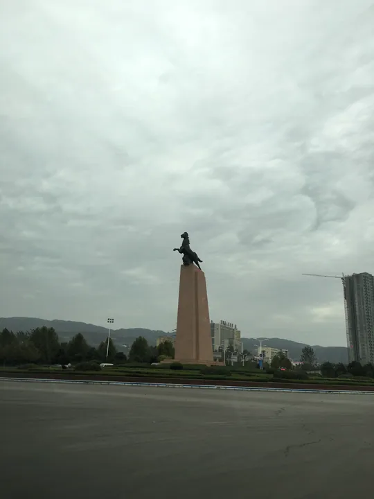 A bronze rearing-horse statue on a tall stone pedestal with city buildings and mountains behind