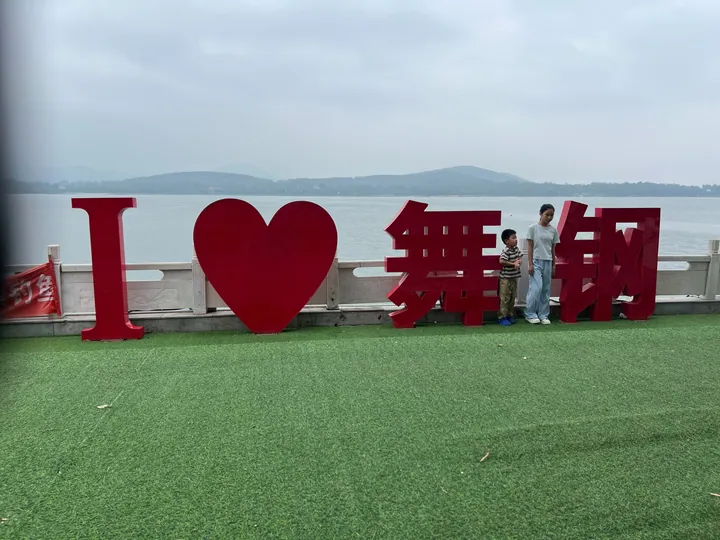 Large red letters spelling 'I love Wugang' beside a lake with hills behind
