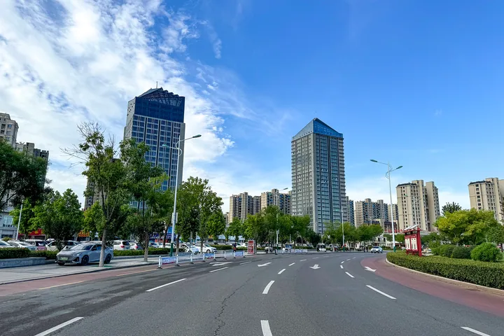 A wide city street lined with modern high-rise buildings in Minquan County