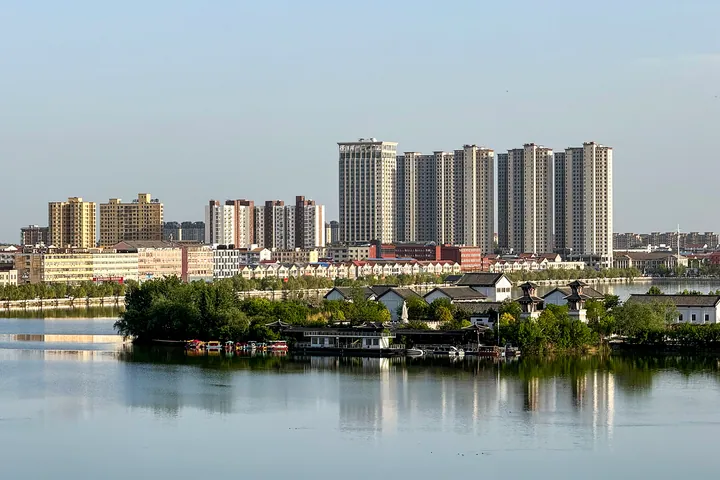 High-rise apartment towers and low traditional-style buildings reflected in a lake in Sui County