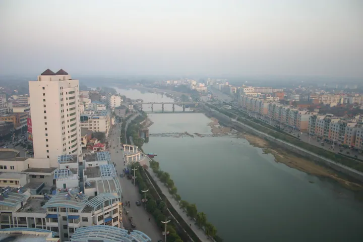 Riverside buildings and a bridge seen from an elevated viewpoint in Huangchuan County
