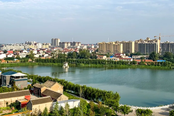 A lake reflecting the city skyline under a clear sky in Xihua County