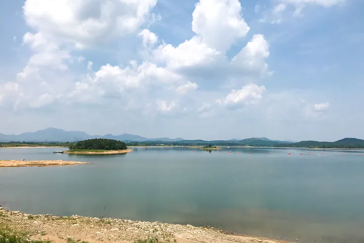 A reservoir surrounded by hills under a partly cloudy sky in Biyang County
