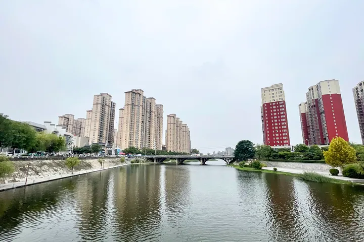 A river reflecting apartment towers and a bridge in Runan County