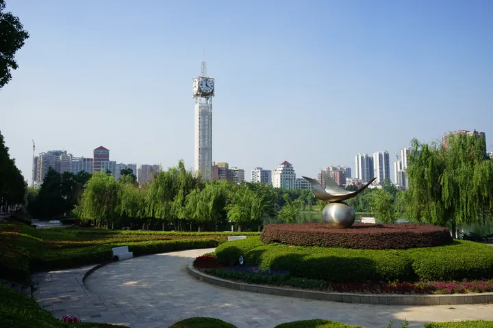 A clock tower and sculpture in a park with the city skyline behind