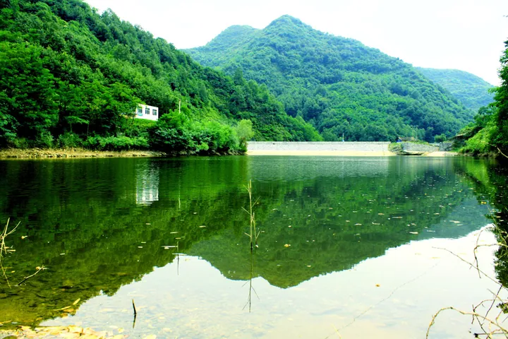 A mountain reservoir with still green water reflecting the surrounding hills in Yunxi County