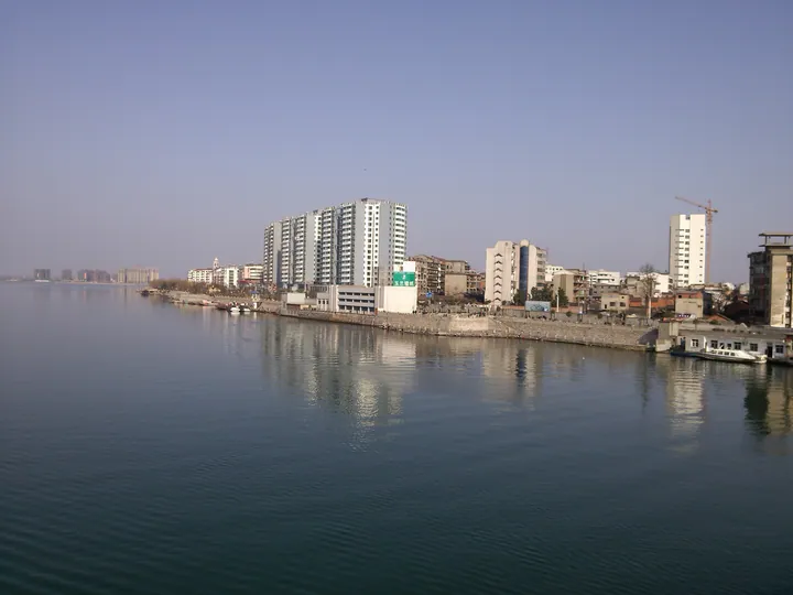 Riverside buildings reflected in calm water under a clear sky in Laohekou