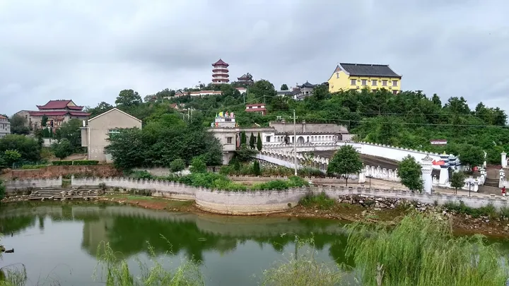 Temple buildings and a pagoda on a hill above a pond in Huangmei County