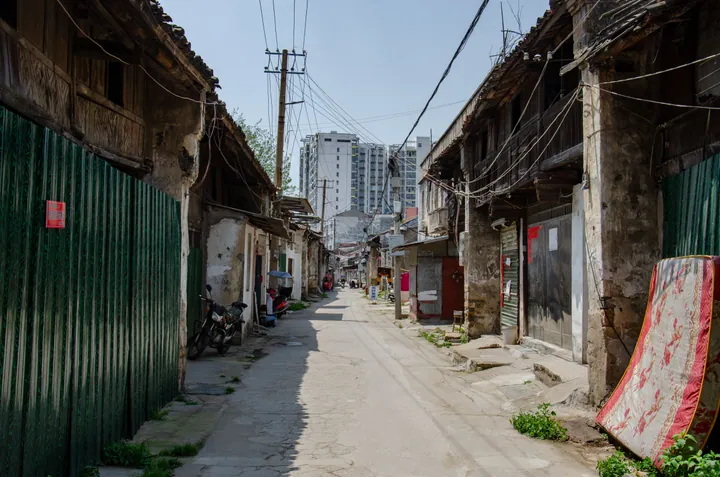 A narrow old town street with traditional buildings and a modern high-rise in the background, Guangshui