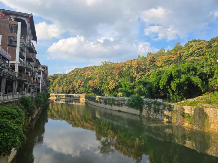 Traditional riverside buildings and colourful autumn trees reflected in a calm river in Laifeng