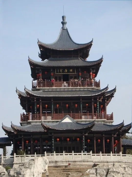 Multi-tiered traditional Chinese pavilion tower with red lanterns, set against a blue sky
