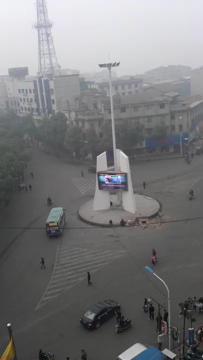 An elevated view of a hazy town square roundabout with a bus and pedestrians in Xiangyin County