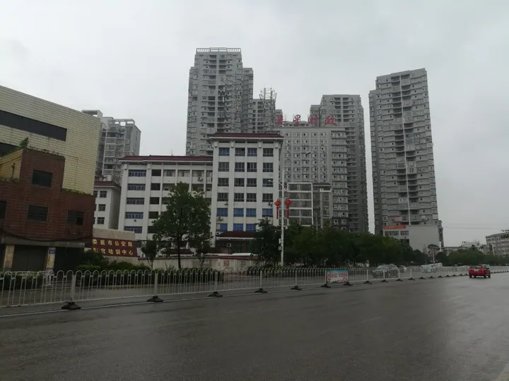 A rainy city street with high-rise apartment buildings and a government office building