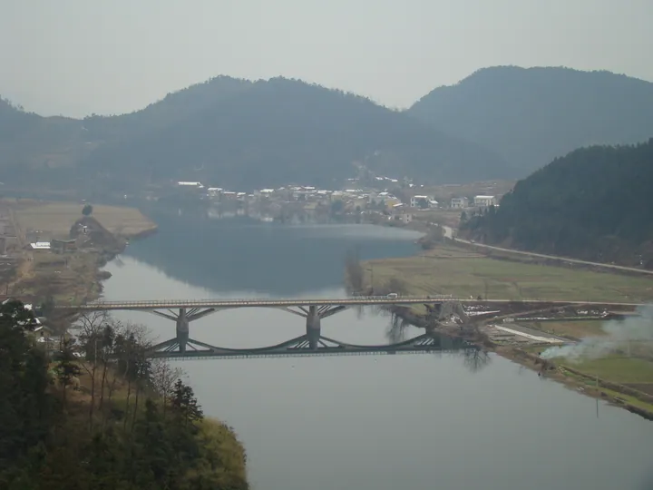 A road bridge crossing a river with a riverside town and hills behind, in Shuangfeng County