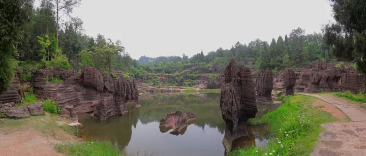 Reddish karst rock pinnacles reflected in a still pond surrounded by forest