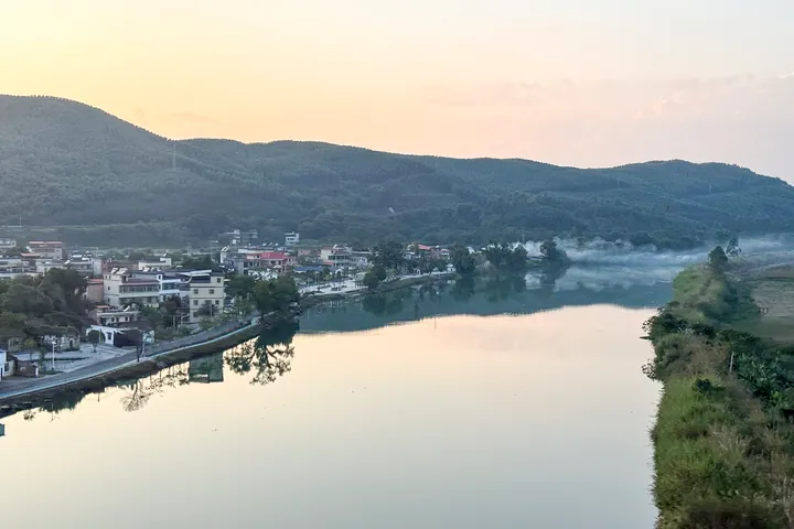 A calm river reflecting the sunset sky beside a small riverside town with hills behind