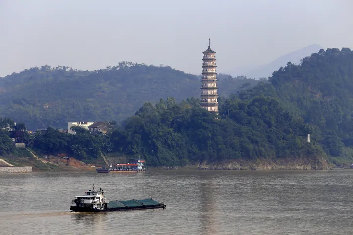 The tiered Sanyuan Pagoda reflected in a river, with a cargo boat passing in Deqing County