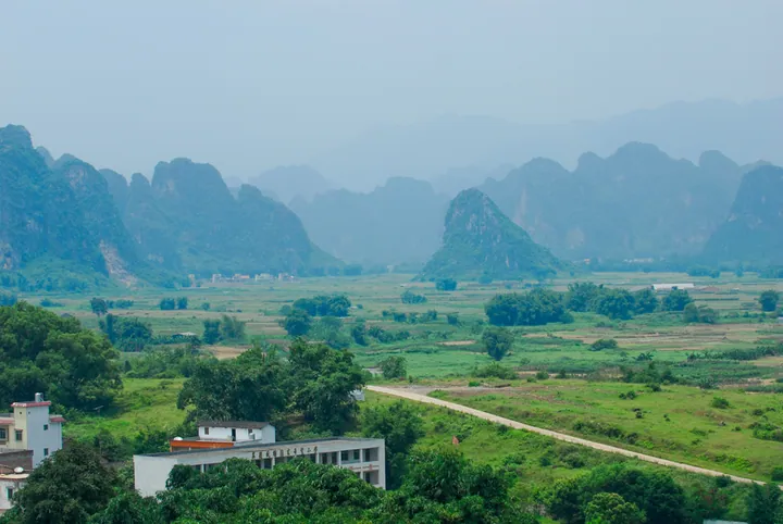 Hazy karst peaks rising above fields and a village building in Yingde