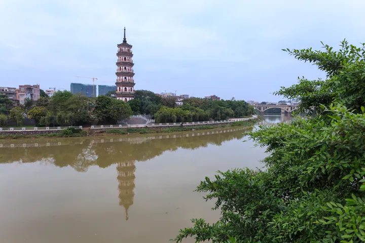 The tiered Luoding Wen Pagoda reflected in a river, with a bridge in the background