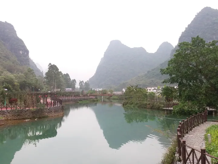 A riverside walkway with karst hills and a village in the background