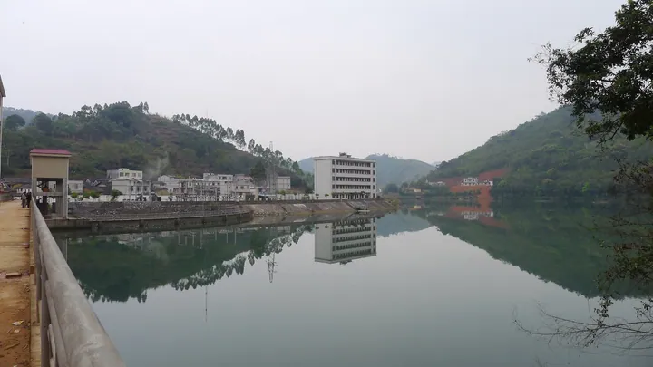 A reservoir with a multi-storey building and hills reflected in the calm water