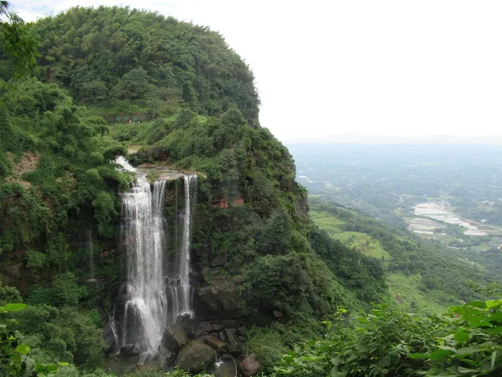 A waterfall cascading down a cliff above a green valley near Nanxi District, Yibin