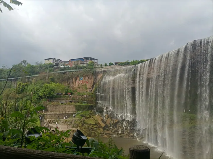 A wide waterfall cascading over a cliff with a viewing platform in Yuechi County