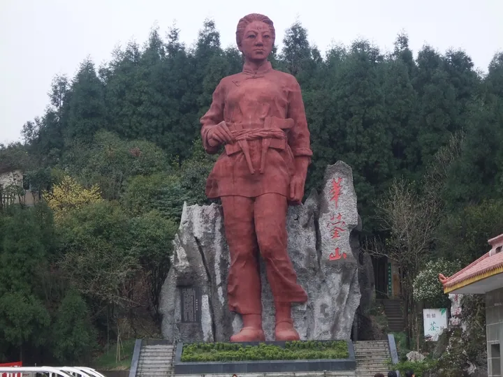 A red statue of a woman in front of a rock inscribed with 'Huaying Mountain' at a scenic area gate